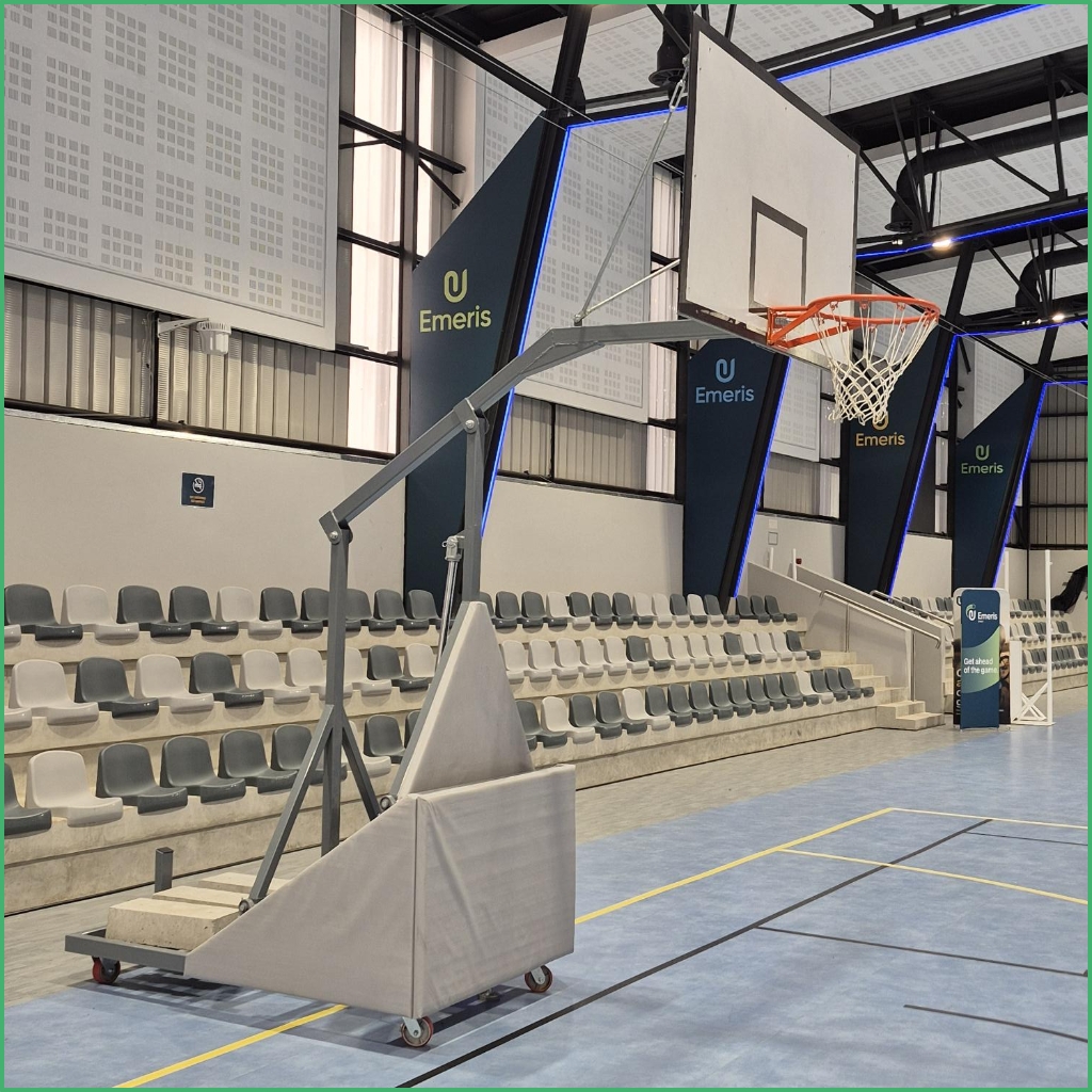 Synsport sports equipment - Basketball Folding Club 4 | Synsport Indoor basketball gym with a portable freestanding backboard and hoop, wheeled base, and bleacher seating along the wall.