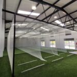 Synthetic Cricket Facilities SACS Indoor Nets | Synsport Indoor sports facility featuring a long netted enclosure over artificial turf with white field markings and industrial ceiling lights.