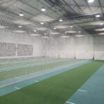 Synthetic Cricket Facilities Western Province | Synsport Indoor sports facility with long netted practice lanes and green turf, white partition curtains at the far end.