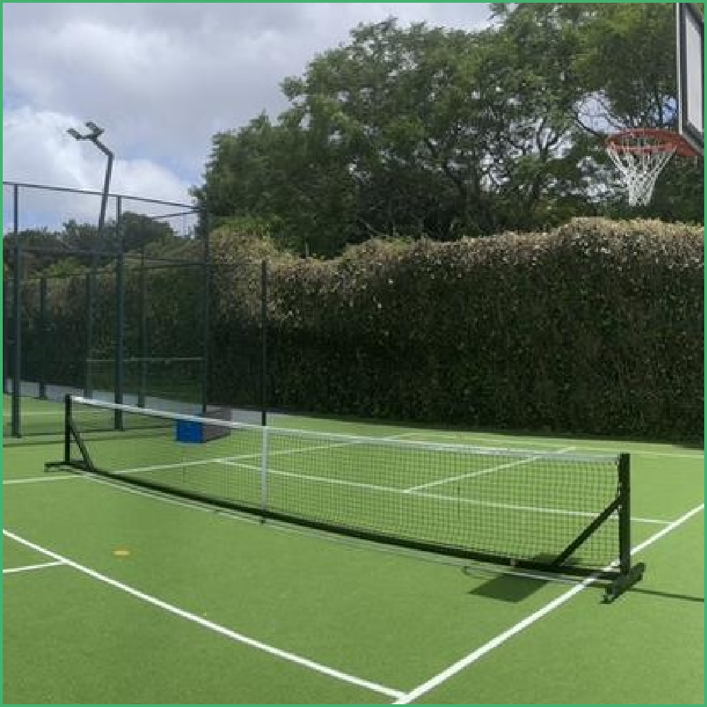Synsport sports equipment - Free standing pickleball posts and net 1 | Synsport Outdoor tennis court with a net, green surface and surrounding hedges and fencing.