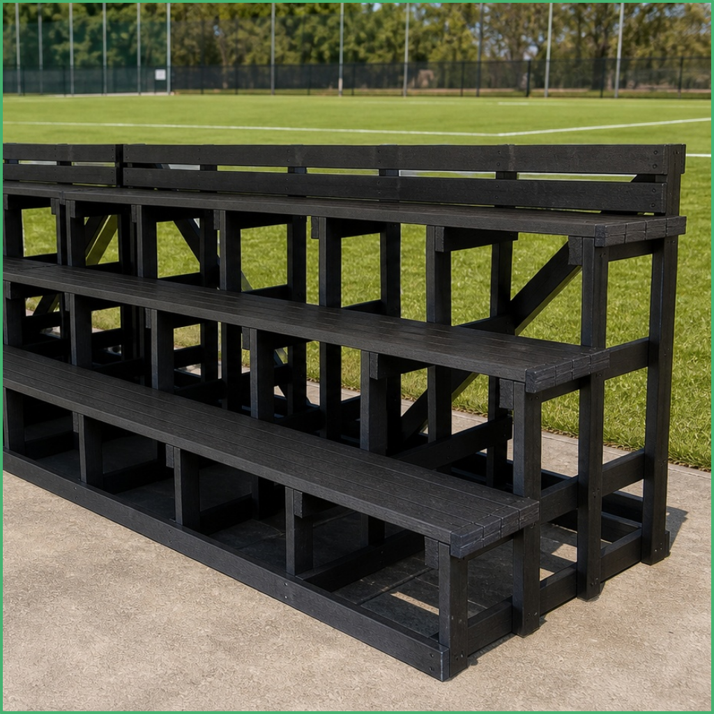 Synsport sports equipment - Recycled plastic seating Featured | Synsport Black wooden bleachers stacked beside a grassy sports field with a fence in the background.
