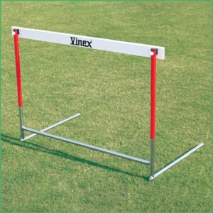 Athletic hurdle on a grassy field with red vertical posts and a white crossbar labeled 'Vinex' for jump training